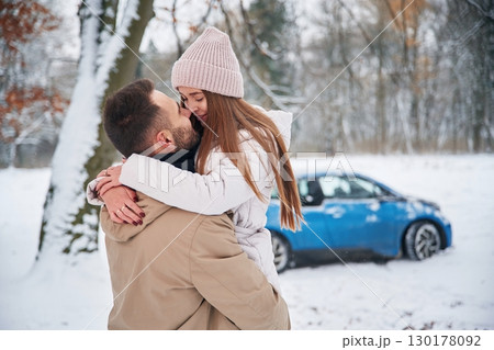Smiling, having fun. Happy couple having a walk in winter forest. Blue car is parked 130178092