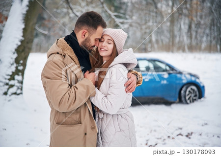 Smiling, having fun. Happy couple having a walk in winter forest. Blue car is parked 130178093