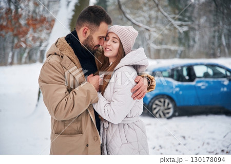 Smiling, having fun. Happy couple having a walk in winter forest. Blue car is parked 130178094