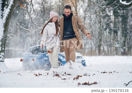 Front view, having fun. Happy couple having a walk in winter forest. Blue car is parked Front view, having fun. Happy couple having a walk in winter forest. Blue car is parked 130178116