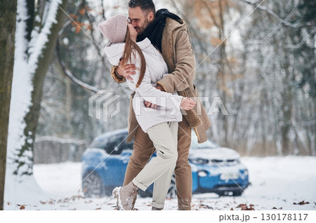 Blue car is parked behind. Happy couple having a walk in winter forest Blue car is parked behind. Happy couple having a walk in winter forest 130178117