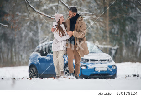 Lovely people. Happy couple having a walk in winter forest. Blue car is parked Lovely people. Happy couple having a walk in winter forest. Blue car is parked 130178124