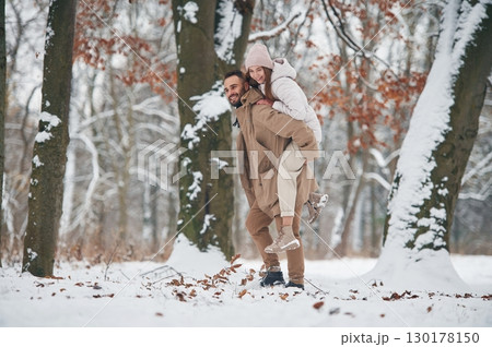 Woman is riding on the man. Lovely couple have a walk in the winter forest 130178150