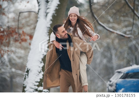 Playful mood. Happy couple having a walk in winter forest. Blue car is parked Playful mood. Happy couple having a walk in winter forest. Blue car is parked 130178155