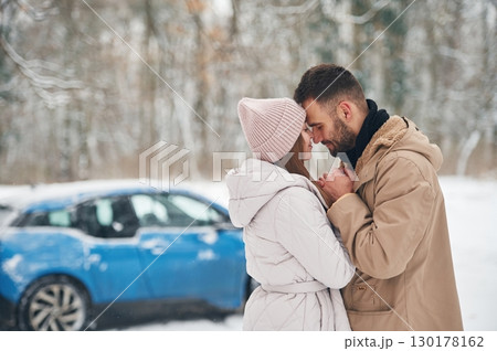 Happy couple having a walk in winter forest. Blue car is parked Happy couple having a walk in winter forest. Blue car is parked 130178162