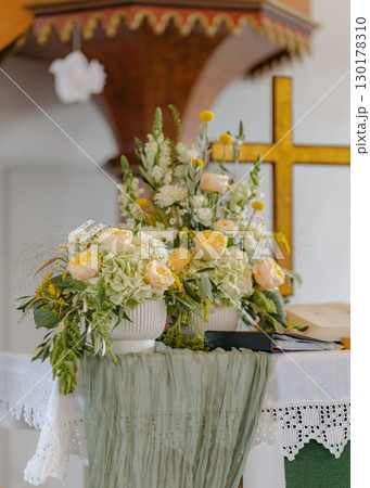 Beautiful floral arrangement with roses and hydrangeas decorates a church altar, complemented by a fabric drape. The setup includes a cross and open book, symbolizing a spiritual setting Beautiful floral arrangement with roses and hydrangeas decorates a church altar, complemented by a fabric drape. The setup includes a cross and open book, symbolizing a spiritual setting 130178310
