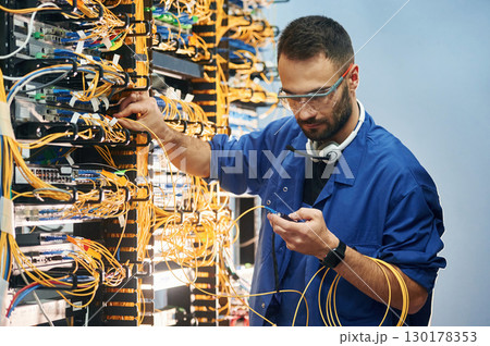 Checking signal by device. Young man is working with internet equipment and wires in server room 130178353