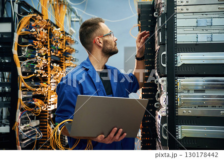Young man is working with internet equipment and wires in server room 130178442