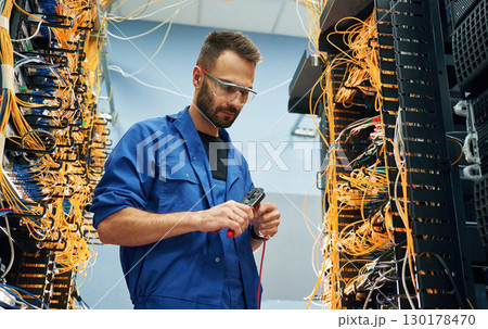 Busy by cutting the wire. Young man is working with internet equipment in server room Busy by cutting the wire. Young man is working with internet equipment in server room 130178470