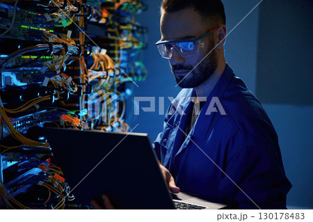 In glasses. Young man is working with internet equipment and wires in server room In glasses. Young man is working with internet equipment and wires in server room 130178483