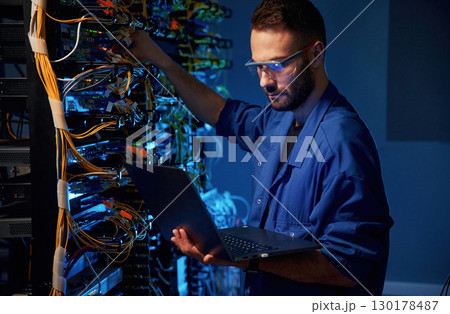 In glasses. Young man is working with internet equipment and wires in server room In glasses. Young man is working with internet equipment and wires in server room 130178487