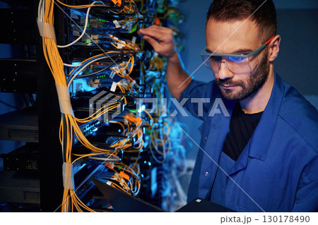 In glasses. Young man is working with internet equipment and wires in server room In glasses. Young man is working with internet equipment and wires in server room 130178490