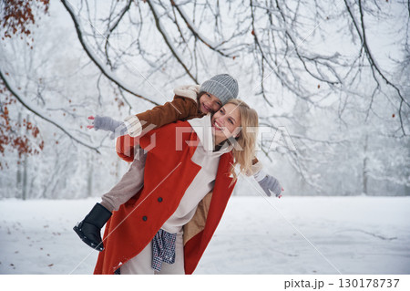 Holding girl by hands on spine. Mother and her daughter is on the winter meadow and forest 130178737