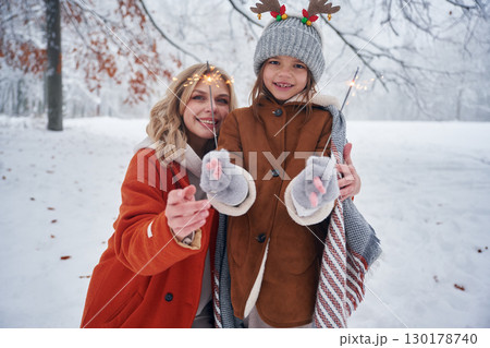 Holding sparklers, new year. Mother and her daughter is on the winter meadow and forest 130178740