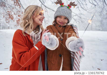 Holding sparklers, new year. Mother and her daughter is on the winter meadow and forest 130178742