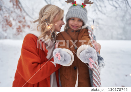 Holding sparklers, new year. Mother and her daughter is on the winter meadow and forest Holding sparklers, new year. Mother and her daughter is on the winter meadow and forest 130178743