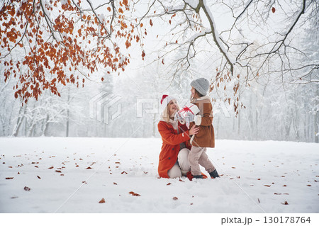 In Santa clothes, with gift box. Mother and her daughter is on the winter meadow and forest 130178764