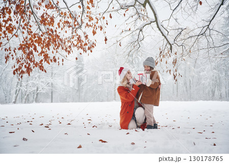 In Santa clothes, with gift box. Mother and her daughter is on the winter meadow and forest 130178765