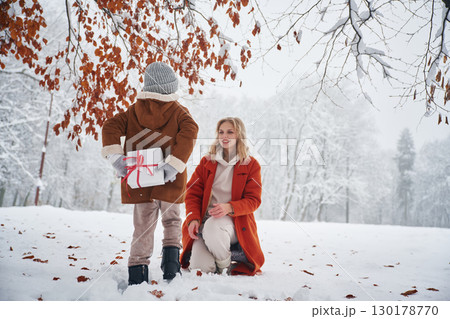 Girl is holding gift box for woman, behind her. Mother and her daughter is on the winter meadow and forest Girl is holding gift box for woman, behind her. Mother and her daughter is on the winter meadow and forest 130178770