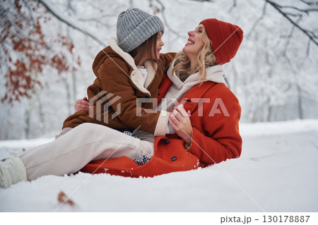 Sitting on the ground. Mother and her daughter is on the winter meadow and forest Sitting on the ground. Mother and her daughter is on the winter meadow and forest 130178887