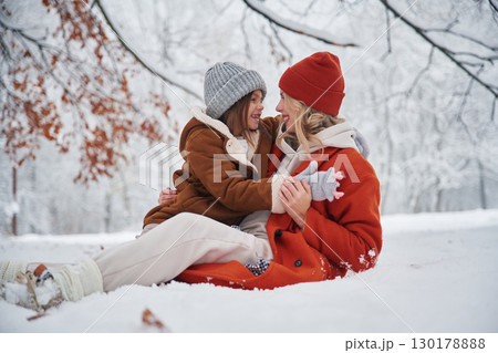 Sitting on the ground. Mother and her daughter is on the winter meadow and forest 130178888