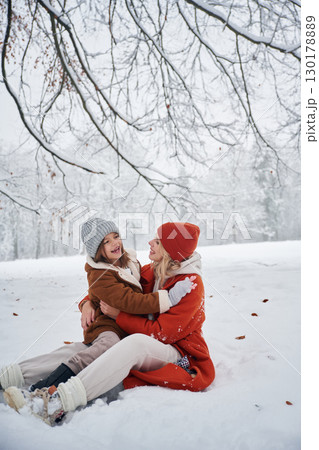 Sitting on the ground. Mother and her daughter is on the winter meadow and forest 130178889