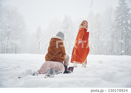 Sled ride. Mother and her daughter is on the winter meadow and forest Sled ride. Mother and her daughter is on the winter meadow and forest 130178924
