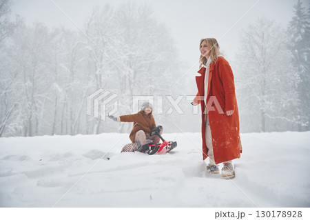 A woman pulls a sled. Mother and her daughter is on the winter meadow and forest 130178928