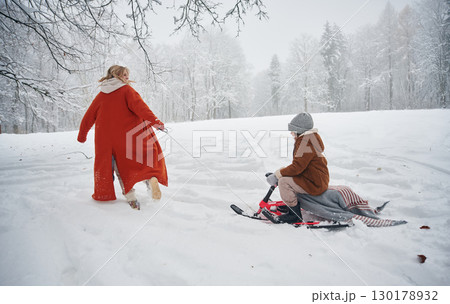 A woman pulls a sled. Mother and her daughter is on the winter meadow and forest 130178932
