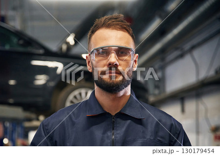 Looking at the camera. Car repairman is in the garage with automobile 130179454