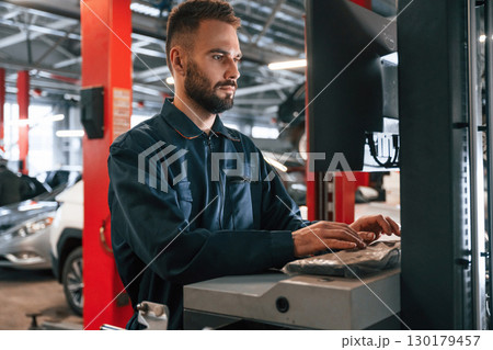 Working by computer. Car repairman is in the garage with automobile Working by computer. Car repairman is in the garage with automobile 130179457