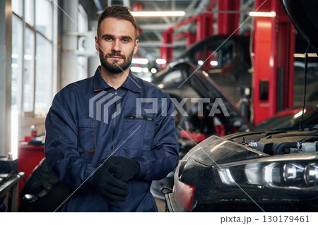 Wearing the gloves, standing. Car repairman is in the garage with automobile Wearing the gloves, standing. Car repairman is in the garage with automobile 130179461
