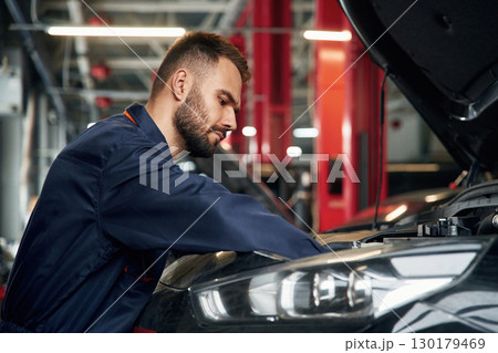 Busy car repairman is in the garage with automobile, fixing it 130179469