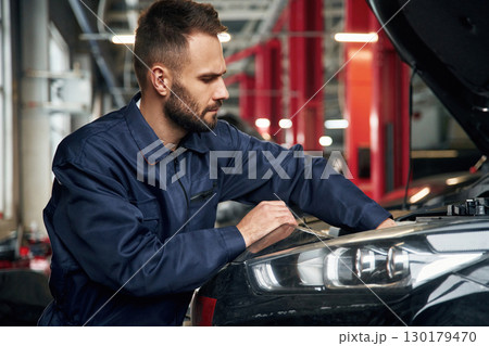 Busy car repairman is in the garage with automobile, fixing it 130179470
