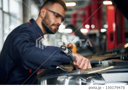 Professional electro device in hands. Car repairman is in the garage with automobile Professional electro device in hands. Car repairman is in the garage with automobile 130179478