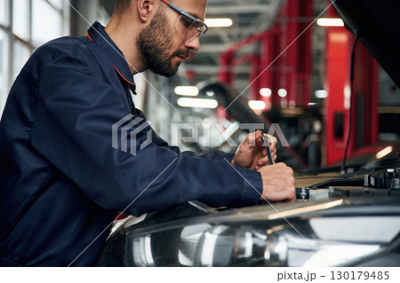 Hood is opened, fixing. Car repairman is in the garage with automobile 130179485