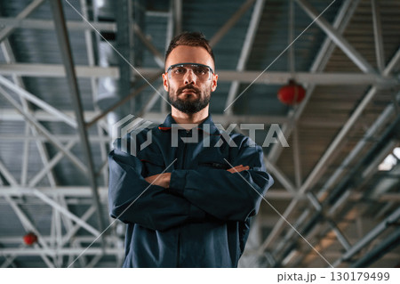 Standing and posing. Car repairman is in the garage with automobile 130179499