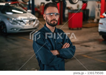 Standing and posing. Car repairman is in the garage with automobile Standing and posing. Car repairman is in the garage with automobile 130179500