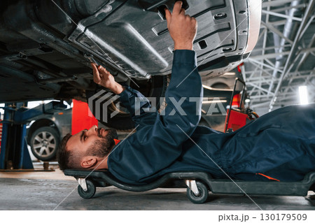 Lying down on the ground. Car repairman is in the garage with automobile Lying down on the ground. Car repairman is in the garage with automobile 130179509