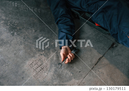 Repairman is lying down on the ground with tool in hand 130179511