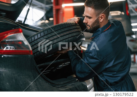 Holding a tire. Car repairman is in the garage with automobile Holding a tire. Car repairman is in the garage with automobile 130179522