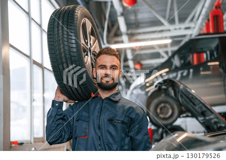 Holding a tire. Car repairman is in the garage with automobile Holding a tire. Car repairman is in the garage with automobile 130179526