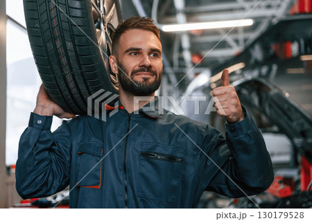 Holding a tire. Car repairman is in the garage with automobile Holding a tire. Car repairman is in the garage with automobile 130179528