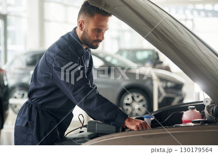 With device for measuring electricity. Car repairman is in the garage with automobile With device for measuring electricity. Car repairman is in the garage with automobile 130179564