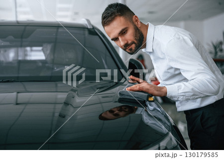 Looking at polished surface. Worker in formal clothes is in the auto salon 130179585