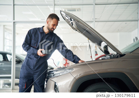 Device for measuring voltage is in hands. Car repairman is in the garage with automobile 130179611