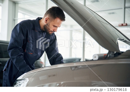 Side view, hood is opened. Car repairman is in the garage with automobile 130179618