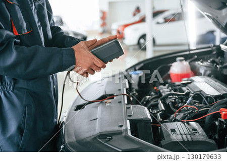 Device for measuring voltage is in hands. Car repairman is in the garage with automobile 130179633