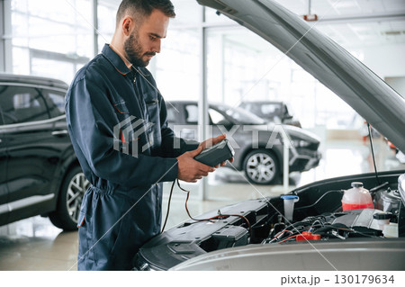 Device for measuring voltage is in hands. Car repairman is in the garage with automobile 130179634