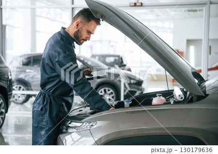 View from the side. Car repairman is in the garage with automobile View from the side. Car repairman is in the garage with automobile 130179636